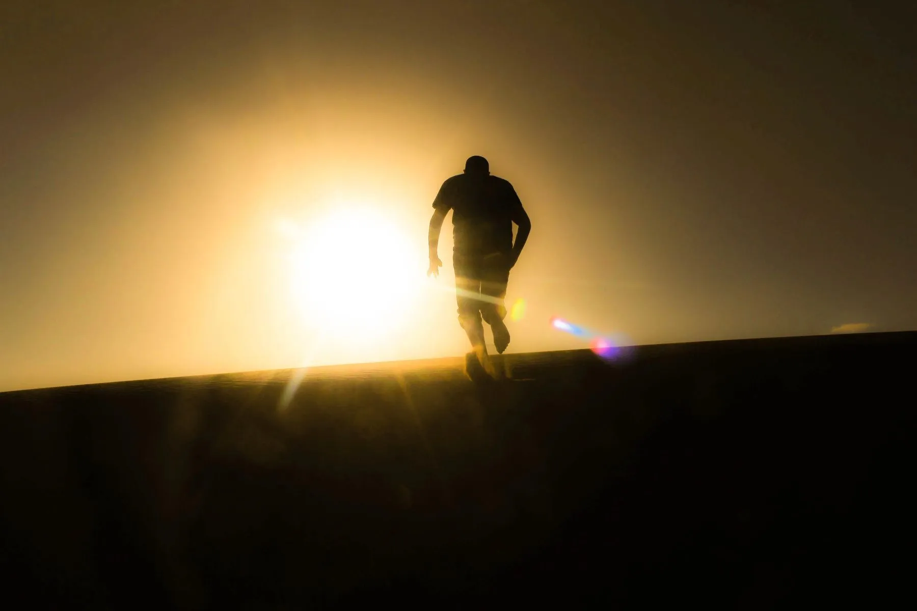 Runner climbing a dark ridge toward the rising sun
