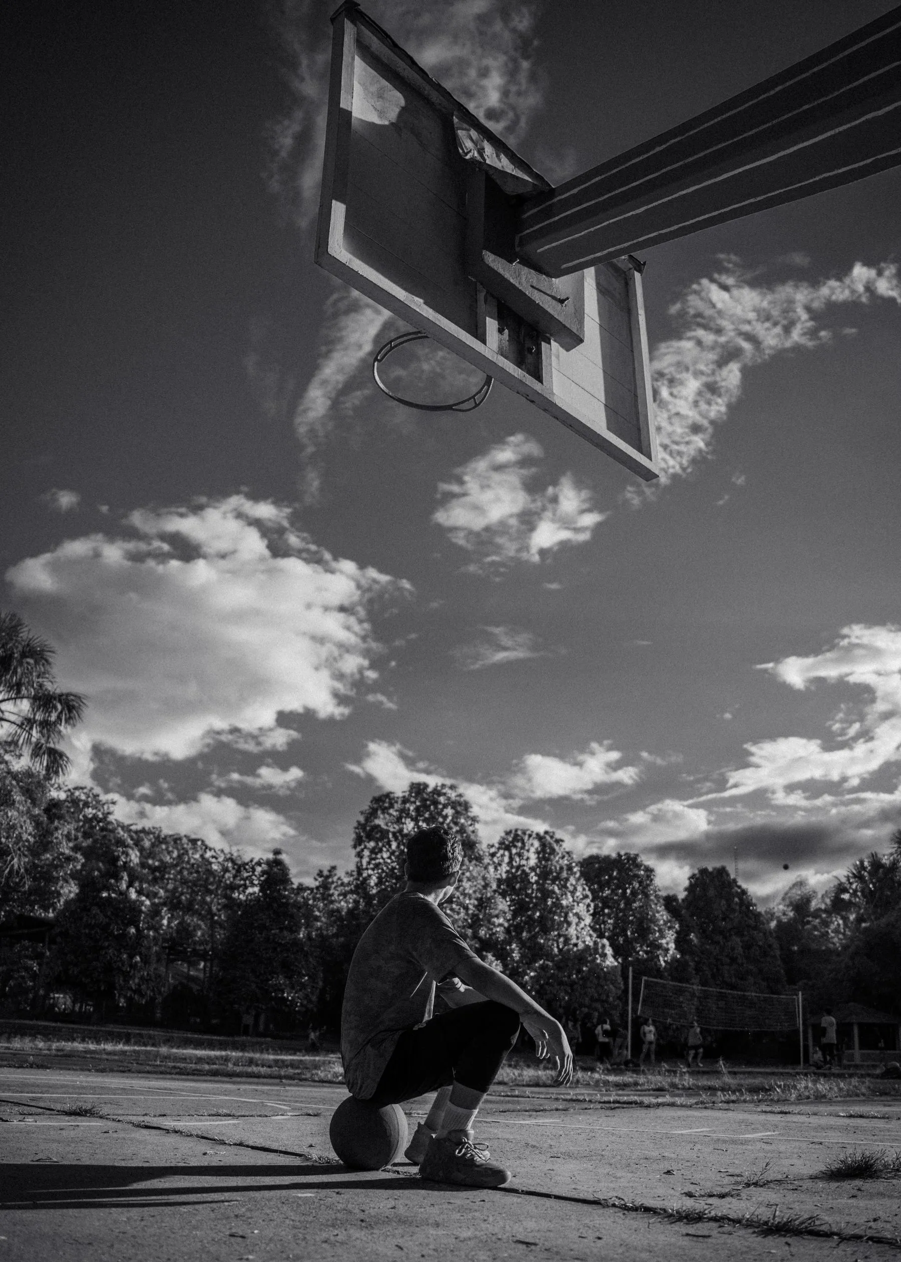 Basketball player sitting alone on his ball, looking up at the hoop